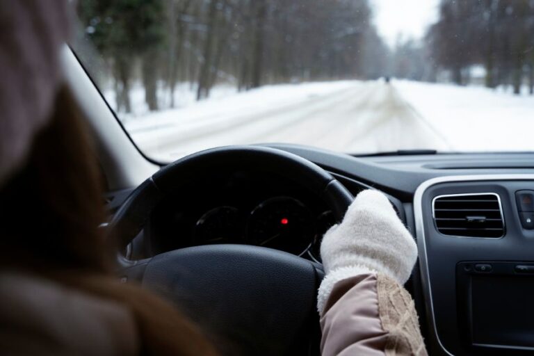 Close-up of a driver holding the steering wheel while driving on a snowy Canadian road, highlighting winter driving safety tips.
