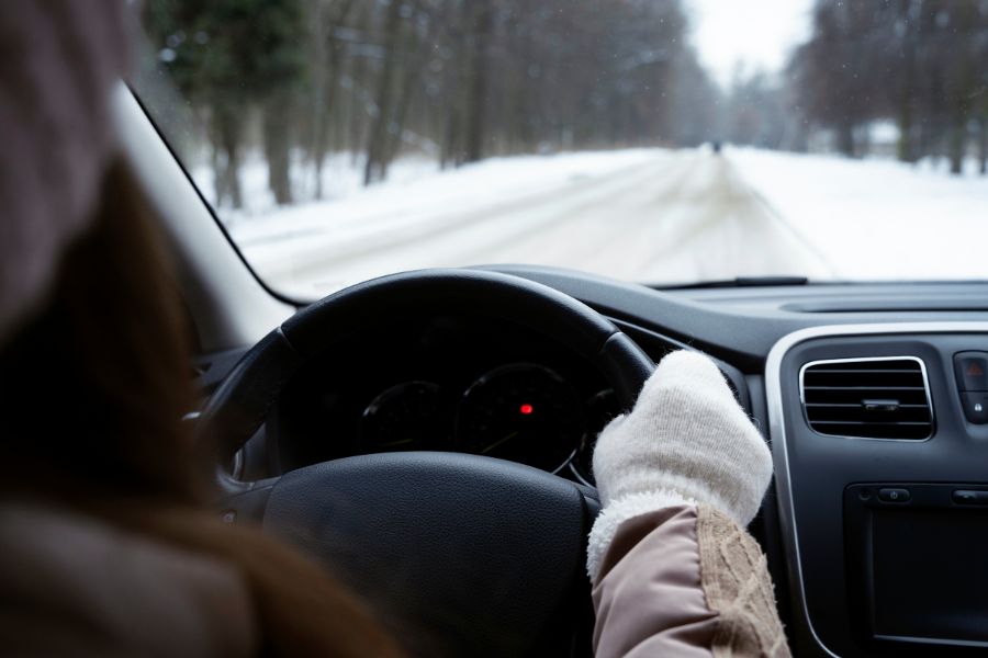 Close-up of a driver holding the steering wheel while driving on a snowy Canadian road, highlighting winter driving safety tips.