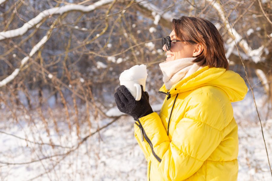 Weather forecaster in a yellow jacket holding a mug of snow during a winter field observation.